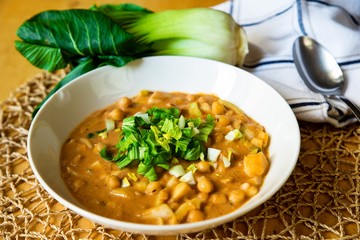 Chickpease soup, pak choi, towel and spoon on table.