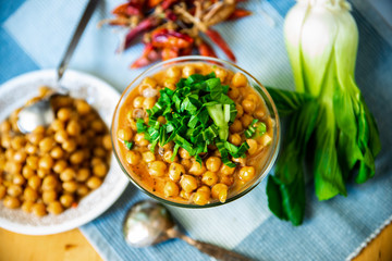 Boiled chickpeas in bowl and plate, pak choi, chilli peppers on table.