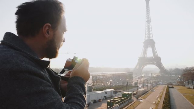 Rear view happy freelance photographer man taking a picture of Eiffel Tower in Paris with retro film camera slow motion.