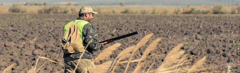 A man with a gun in his hands and an green vest on a pheasant hunt in a wooded area in cloudy...