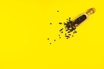 Spice scoop / spoon with black peppercorns on yellow background