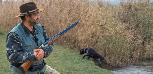 Hunting period, autumn season open. A hunter with a gun in his hands in hunting clothes in the autumn forest in search of a trophy. A man stands with weapons and hunting dogs tracking down the game.