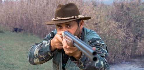 Fototapeta premium Hunting period, autumn season open. A hunter with a gun in his hands in hunting clothes in the autumn forest in search of a trophy. A man stands with weapons and hunting dogs tracking down the game.