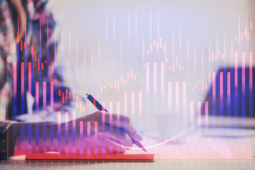 A woman hands writing information about stock market in notepad. Forex chart holograms in front. Concept of research. Double exposure