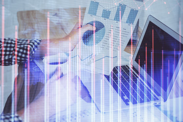 Double exposure of stock graph with businessman typing on computer in office on background. Concept of hard work.