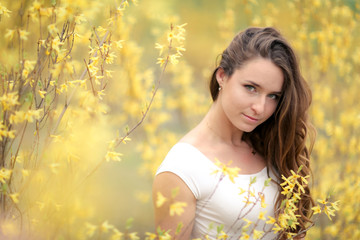 Portrait of a woman in a white dress on a background of yellow bushes with flowers.