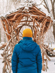 Fototapeta premium A man in a yellow winter hat walks through a fabulous winter town, a carved house, a woodworker