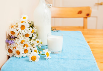 Simply stylish wooden kitchen with bottle of milk and glass on table, summer flowers camomile, healthy foog moring concept close up