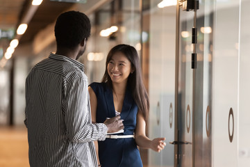 Smiling millennial multiracial colleagues talk in office hallway