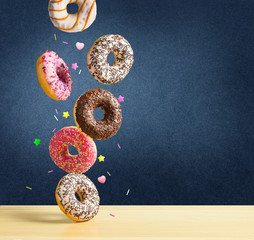 Flying donuts. Mix of multicolored sweet doughnuts with sprinkel falling on the table on dark blue...