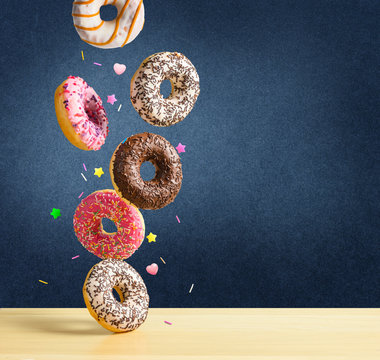 Flying donuts. Mix of multicolored sweet doughnuts with sprinkel falling on the table on dark blue textured background.