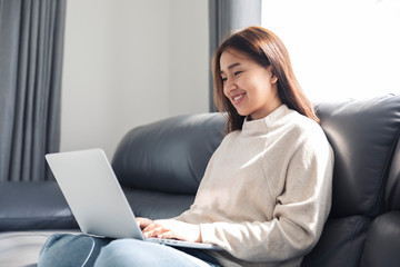 Naklejka premium Young woman doing research work for her business, Smiling woman sitting on sofa relaxing while browsing online shopping website