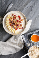Healthy cereal breakfast, oatmeal topped with banana slices, dried cranberries, walnut, served with honey