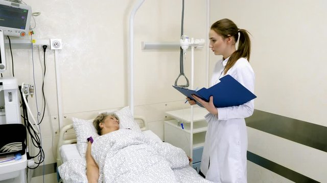 Caring medical worker in hospital talking to elderly woman at her bedside. 4K