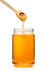 Honey wooden spoon above glass jar, on white background