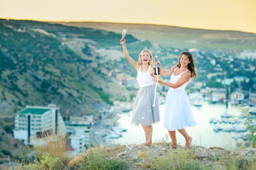 Two happy young women drinking together and having fun on top of a mountain.