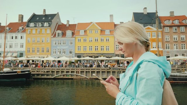 Woman uses smartphone on background Nyhavn canal, against the background of famous colorful houses.