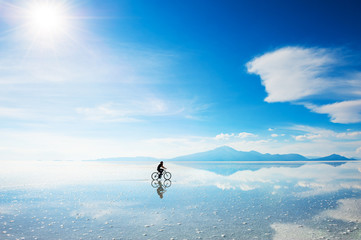 Woman riding a bicycle on the Salar de Uyuni salt flat in Bolivia. South America landscapes