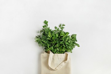 A bunch of fresh organic greenery parsley and dill in a cotton reusable bag on a white background. Healthy food, organic products, eco friendly lifestyle, zero waste concept. Top view, copy space.