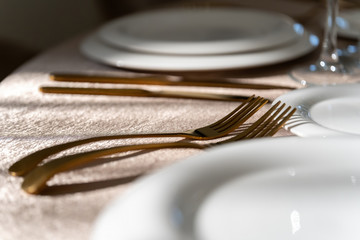 Chic and elegant, gold-plated cutlery and white plates, table setting with empty plates. Macro.