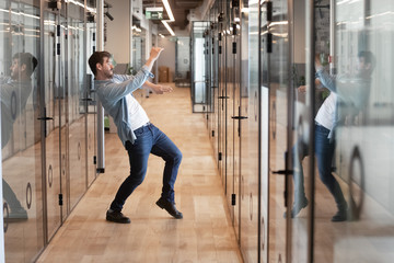 Obraz premium Funny millennial male dancing in hallway celebrating success