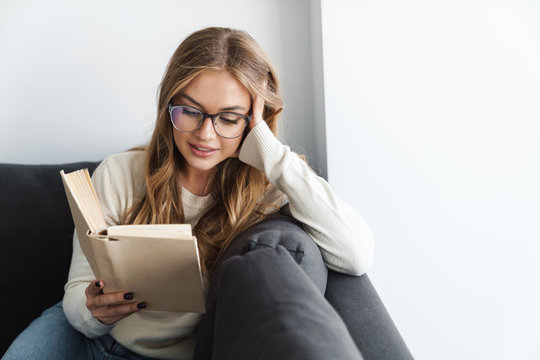 Photo Of Young Pleased Woman Reading Book While Sitting On Couch