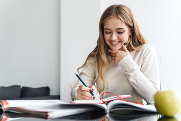 Photo of young happy woman smiling and making notes in exercise book