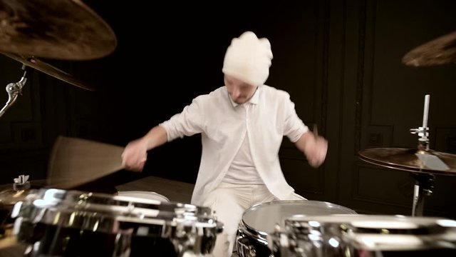 Handsome guy in white actively plays on drum kit in on black background. Closeup