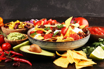 mexican nacho chips garnished with ground beef, guacamole, melted cheese, peppers and cilantro leaves in plate