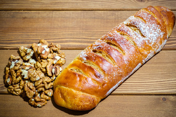 Fresh roll with walnuts and icing sugar on a wooden background. Sweet dessert with nuts on an old table.
