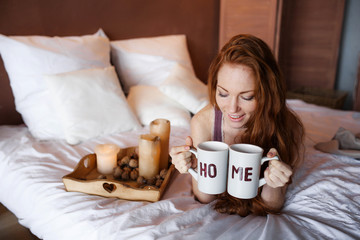 Morning in bed, a young charming red-haired woman with freckles lying in bed, hugging pillow, smiling, enjoying the morning.