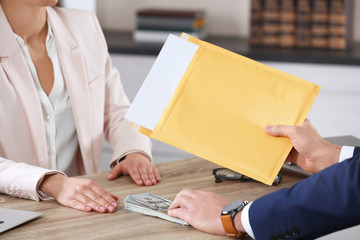 Man offering bribe to woman at table in office, closeup