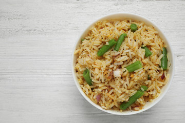 Tasty rice pilaf with vegetables on white wooden table, top view. Space for text