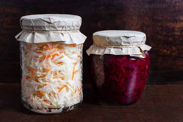 Homemade sauerkraut with carrots and cabbage salad with beets in a glass jar on a brown wooden background.