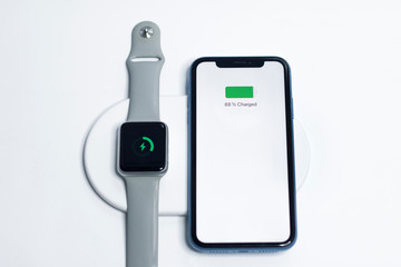 Fototapeta na wymiar Cell mobile smartphone and smartwatches on a new modern wireless charger charging. Easy way to charge fast your gadgets, devices together. Charging battery, recharging without power cables. Connection