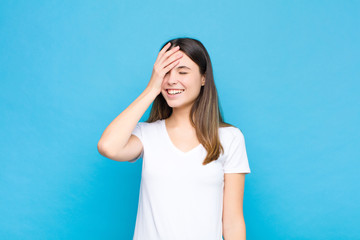 young pretty woman laughing and slapping forehead like saying d‚Äôoh! I forgot or that was a...