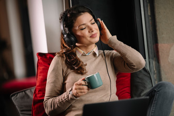 Young woman drinking coffee and listening music. Businesswoman working from home. 