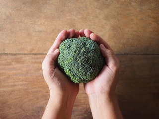 Broccoli in hands on wooden background.