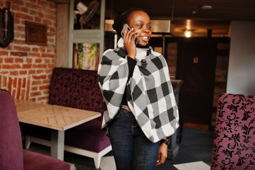 African woman in checkered cape posed at cafe and speak by mobile phone.