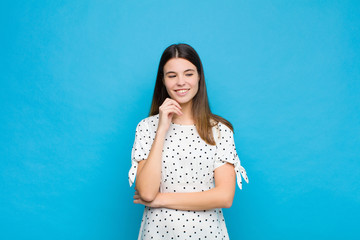 young pretty woman smiling with a happy, confident expression with hand on chin, wondering and...