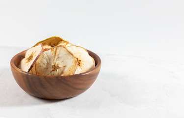 Dried apple chips in a wooden bowl on a white concrete background. Natural organic food.
