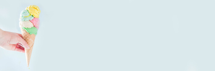 Stack of pastel colorful ice cream scoops in waffle cone, isolated on light blue background. Woman hand holds big ice cream cone with different flavor scoops