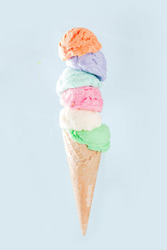 Stack Of Pastel Colorful Ice Cream Scoops In Waffle Cone, Isolated On Light Blue Background. Woman Hand Holds Big Ice Cream Cone With Different Flavor Scoops