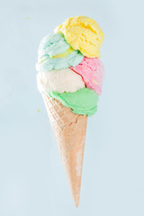 Stack of pastel colorful ice cream scoops in waffle cone, isolated on light blue background. Woman hand holds big ice cream cone with different flavor scoops