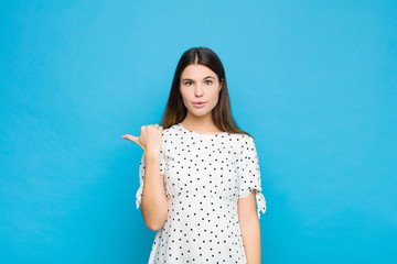 young pretty woman looking astonished in disbelief, pointing at object on the side and saying wow,...