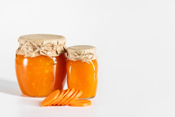 Juicy homemade carrot jam in glass jars on a white background.