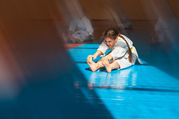 A teenager girl with a yellow belt in karate class is doing stretching. Beautiful morning light. Oriental martial arts. Children's training. © Uladzimir