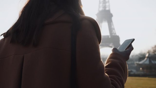 Young beautiful businesswoman using phone messenger app walking at backlit sunny Paris Eiffel Tower view slow motion.