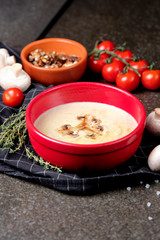 Bowl of mushroom cream soup with fried champignon mushrooms and vegetables on black stone background. Rustic style. Close up.