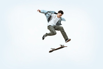Naklejka na ściany i meble Caucasian young skateboarder riding isolated on a white studio background. Man in casual clothing training, jumping, practicing in motion. Concept of hobby, healthy lifestyle, youth, action, movement.